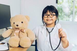 un niño vestido de médico se sienta y examina un oso de peluche en el hospital. foto