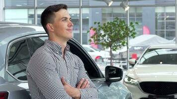 Handsome man smiling dreamily, leaning on a new car at the dealership video