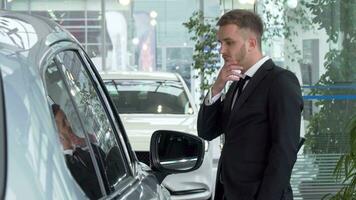 Young businessman in a suit examining cars for sale at the dealership video