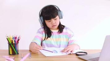 Asian female student wearing headphones studying online from home video