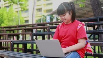 menina dentro vermelho camisa usando computador portátil dentro público parque video