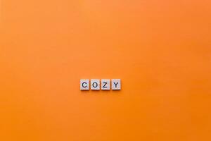 The word cozy made from wooden letters on an orange background. photo