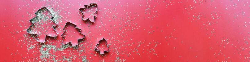 Banner Flay lay molds for cookies in the shape of Christmas trees on a red background with sparkles photo