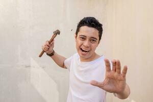 Indonesian men pose hitting, hold the small hammer and wear white tshirt. photo