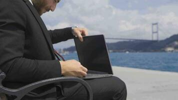 Geschäftsmann Arbeiten auf seine Laptop durch das Meer im das Stadt. schleppend Bewegung. video