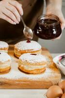 Woman chef prepares fresh donuts with jam at her bakery. Cooking traditional Hanukkah sufganiyot. Small business. photo