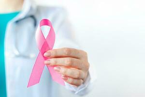 Breast Cancer Awareness Month. Female doctor in medical white uniform holds pink ribbon in her hands. Women's health care photo