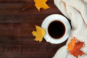 Cup of hot strong coffee and fallen leaves on wooden background.. Autumn morning concept. Warm beverage for cold weather and knitted sweater. photo