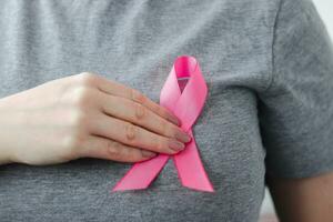 Woman in gray t-shirt attaches pink ribbon to her chest. Breast Cancer Awareness Month. Promoting campaign against cancer. photo