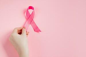 Breast Cancer Awareness Month. Woman's hand holds pink ribbon. Health care concept, cancer control symbol. photo