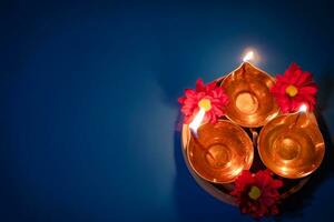 Happy Diwali. Celebrating the Indian Festival of Light. Traditional diya oil lamps and red flowers on blue background photo