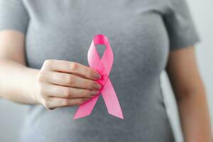 Woman in gray t-shirt holds pink ribbon in her hands. Breast Cancer Awareness Month. Supporting and promoting campaign against cancer. photo