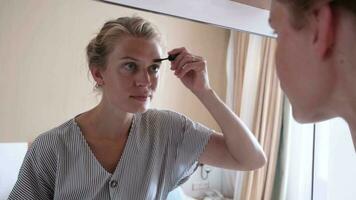 lindo mulher fazer acima de a espelho dentro hotel quarto , escovar sobrancelhas video