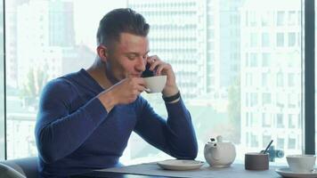 bonito homem desfrutando bebendo chá e falando em a telefone às a restaurante video