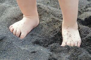 pies de un niño jugando en el negro arena en el playa de tenerife en España en un calentar verano día foto