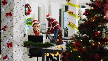 Dolly out portrait shot of happy employee working on christmas season in decorated office. Cheerful worker solving tasks at desk in diverse xmas ornate workplace next to colleagues photo