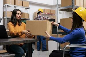 Asian warehouse worker with disability giving package to colleague. Storehouse logistics manager and product picker inspecting order quality and preparing for sending in storage room photo