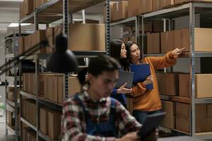 Storehouse asian women employees checking package packing quality in postal storage room. Storehouse shipment operator showing goods in stock on shelf to logistics manager photo