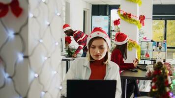 Asian staff member in videocall with teammates during Christmas season in festive decorated office. Employee in teleconference meeting with team in busy xmas ornate workplace photo