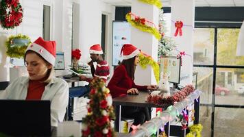 Hardworking multicultural employees working during Christmas season in festive decorated office. Diligent BIPOC coworkers inputing data on computers in diverse xmas ornate workplace photo