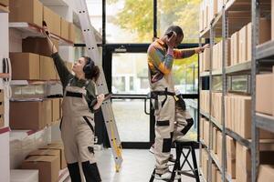 Storage room employee scanning cardboard boxes details using store scanner, looking at checklist during warehouse inventory. Supervisor preparing customers packages working at shipping process photo