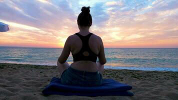 donna praticante yoga a il Alba su il spiaggia. lei è rilassato e sembra a un' panoramico e bellissimo Alba. meditazione e nuovo prospettive video