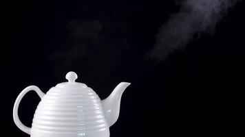 Tea pot on black background with boiling water inside, the steam is rising inthe air video