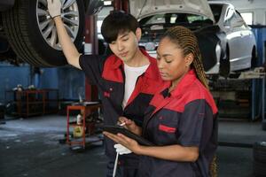 Young Black female inspects repair checklist with automotive mechanic worker partner, quality suspension technician team at fix garage. Vehicle maintenance service works industry occupation jobs. photo