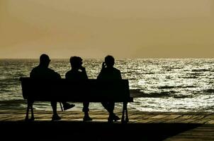 Tres personas sentar en un banco con vista a el Oceano foto