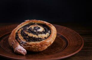 A delicious bun with poppy seeds lies on a clay plate. photo
