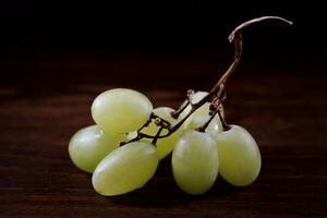 Small bunch of ripe green grapes on a wooden background. photo