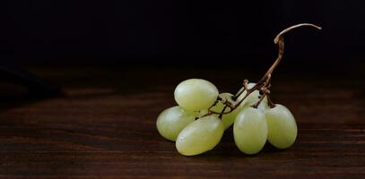 Small bunch of ripe green grapes on a wooden background. photo