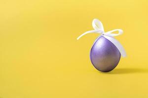 Easter purple egg with a white bow on a yellow background. Closeup copy space. photo