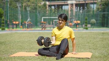 Young man exercising arm muscle with dumbbells. He does sports in the park. video