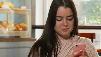 ung kvinna leende, använder sig av henne smart telefon på de kaffe affär video