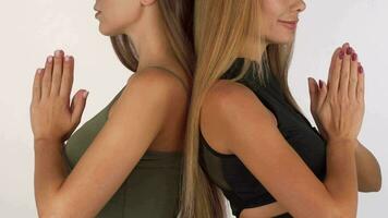 Two women standing back to back putting hands into meditation position video