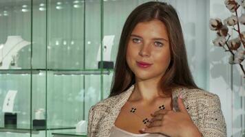 Beautiful young woman looking in the mirror, trying on a necklace at jewelry store video