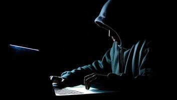 Hooded hacker using a laptop on a dark background. Cybercrime concept. AI Generated. photo