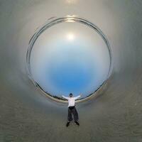 blue hole sphere little planet inside ocean seashore and sands withhappy man stands on coast in rays of evening tropical sun with transformation of spherical panorama 360 degrees. photo