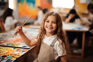 A image of Portrait of a cute little girl with long hair in apron smiling and holding paintbrushes in her hands while standing in art class Generative AI photo