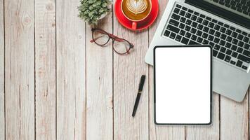 Wooden desk workplace with blank screen tablet, laptop, pen eyeglass and cup of coffee, Top view flat lay with copy space. photo