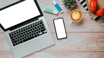 Wooden desk workplace with blank screen laptop and smarphone, headphone, notebook and cup of coffee, Top view flat lay with copy space. photo