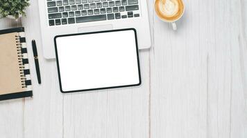 White wooden desk workplace with blank screen tablet, laptop, pen, notebook and cup of coffee, Top view flat lay with copy space. photo