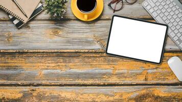 Wooden desk workplace with blank screen tablet, keyboard, mouse,eyeglass, pen, notebook and cup of coffee, Top view flat lay with copy space. photo