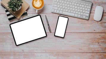 Wooden desk workplace with blank screen tablet and smartphone, pen, keyboard, mouse, notebook and cup of coffee, Top view flat lay with copy space. photo