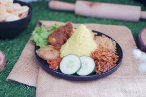 indonesian style yellow rice with chicken and side dishes in black plate on green grass background photo