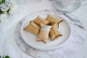 Lepet or Leupeut is a type of snack made from glutinous rice mixed with peanuts, cooked in coconut milk, then wrapped in coconut leaves. Close up view photo