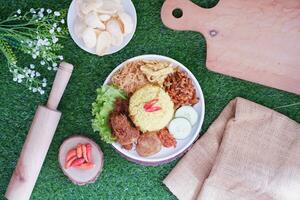 indonesian style yellow rice with minced chicken in white plate on green grass background photo