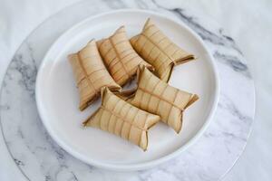 Lepet or Leupeut is a type of snack made from glutinous rice mixed with peanuts, cooked in coconut milk, then wrapped in coconut leaves. Close up view photo