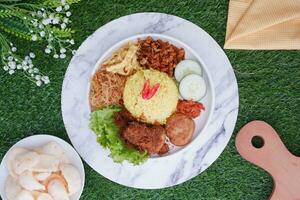 indonesian style yellow rice with minced chicken in white plate on green grass background photo